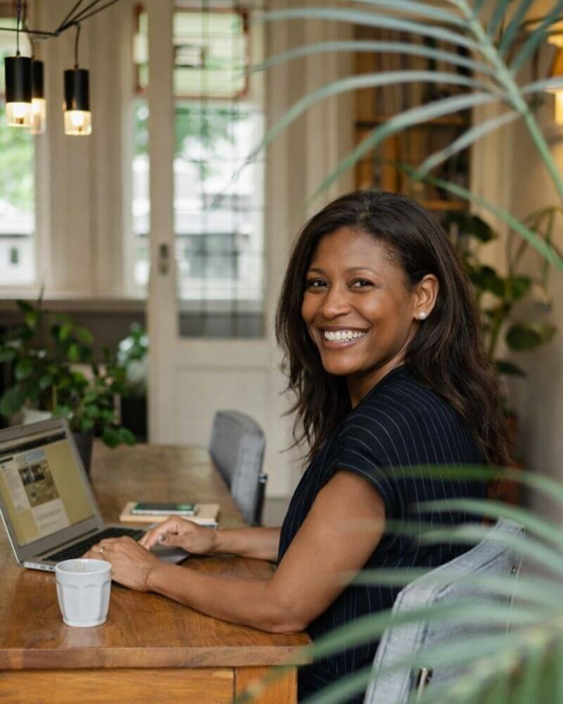 Natalie Broomfield, founder of Dough & Digits Accounting, smiling while working on her laptop in a calm workspace.